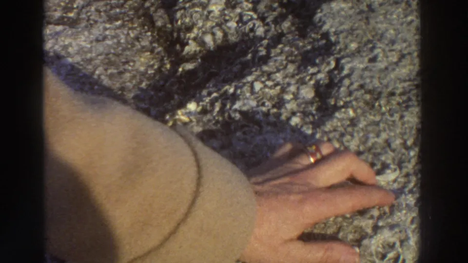 Extreme close-up of a hand wearing a ring touching textured ancient stonework, likely at a Greek archaeological site circa 1976.