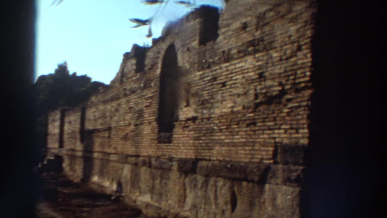 Close-up of layered ancient stone wall with arched opening, filmed on 8mm in Greece, 1976, with pronounced gate vignetting along the left and bottom edges.