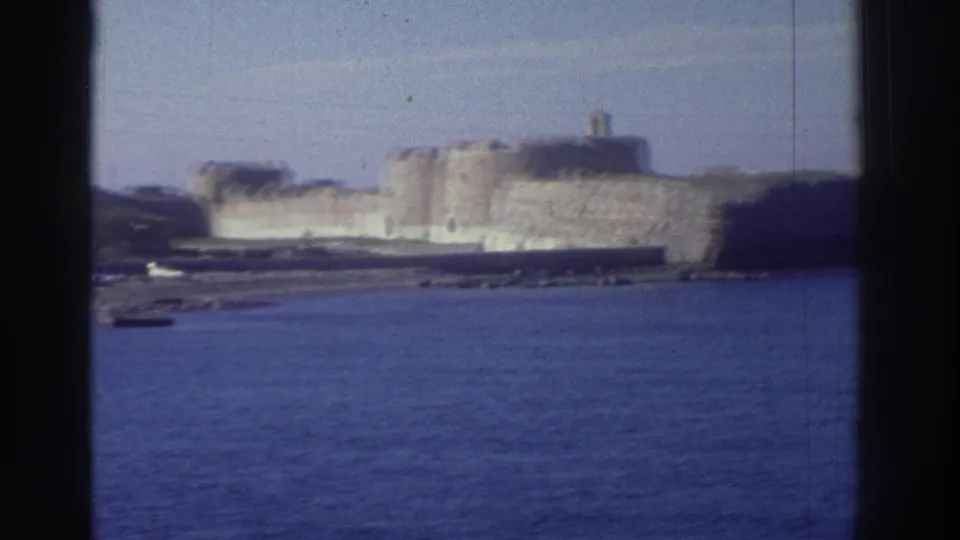 Large stone fortress with circular towers on a rocky coastal promontory, blue Mediterranean sea in foreground, Greece, may be 1976.