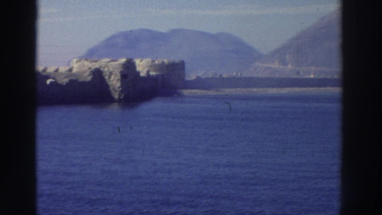 8mm footage from Greece, circa 1976, mid-pan revealing continued fortification walls above the Aegean with a mountain range behind.