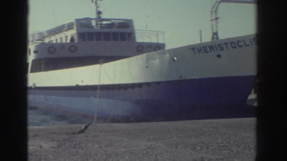 The Greek passenger ferry Themistoclis, white-hulled with multiple passenger decks and lifebuoys, seen from the shoreline in Greece, 1976.