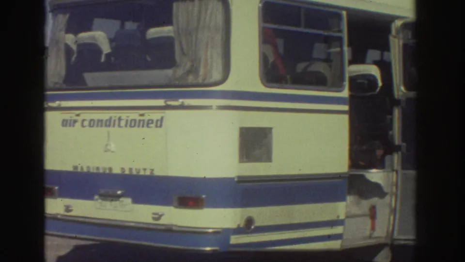 Rear of a cream-and-blue Magirus Deutz tourist coach with 'air conditioned' lettering on the body panel, 8mm home-movie footage from Greece circa 1976.