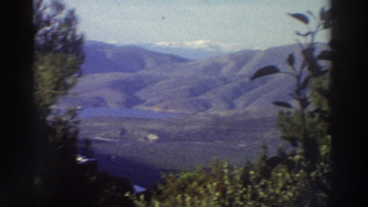 Super 8 frame of a broad mountain landscape with a faint lighter ridge at upper right and trees along the right edge.