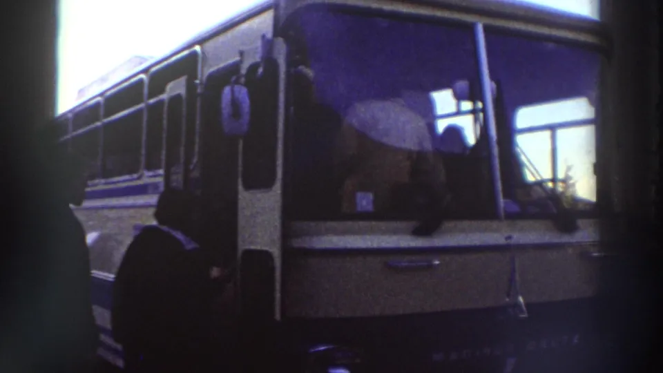 8mm frame showing a touring bus door with silhouetted passengers, filmed in Greece circa 1976, with prominent grain and blue-purple color shift.