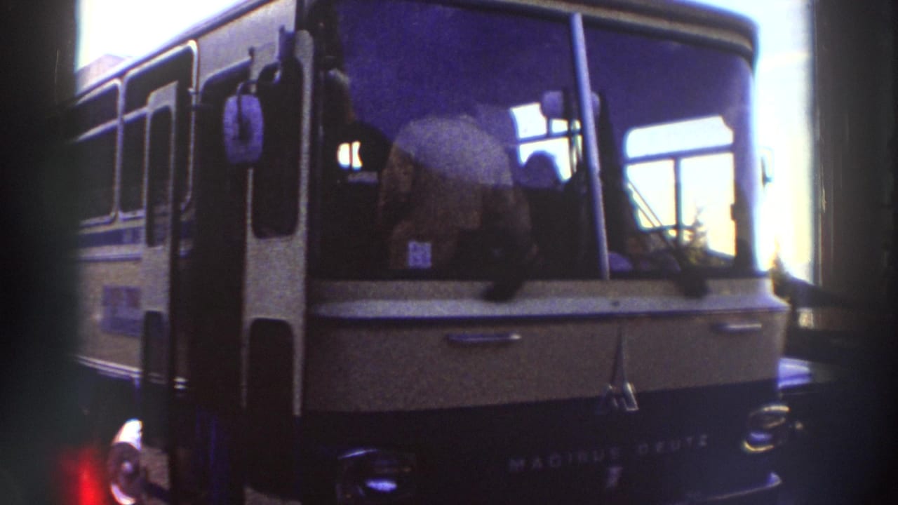 Close-up of a Magirus-Deutz coach bus, dark blue-green body, driver figure visible through windshield, heavy 8mm grain and edge vignetting.