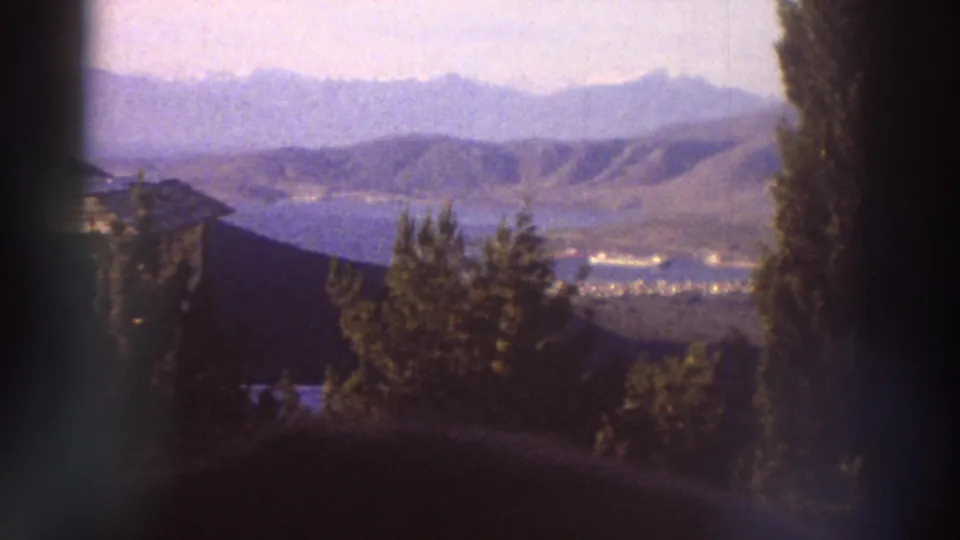 Greek landscape showing rolling hills, tall poplar trees, and a wide valley with a lake in the distance, filmed on 8mm in the mid-1970s with a cool blue color cast.