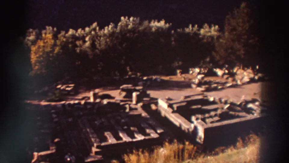 Panned view across scattered stone architectural fragments at a Greek archaeological site, 1976, 8mm home movie with warm amber tones.