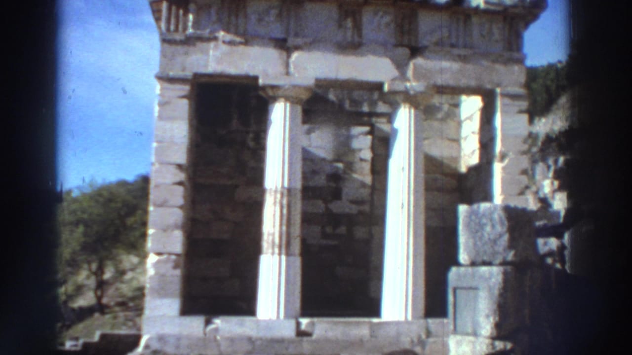 Close-up of an ancient treasury-style building with white Doric columns and carved pediment at an archaeological site in Greece, circa 1976.