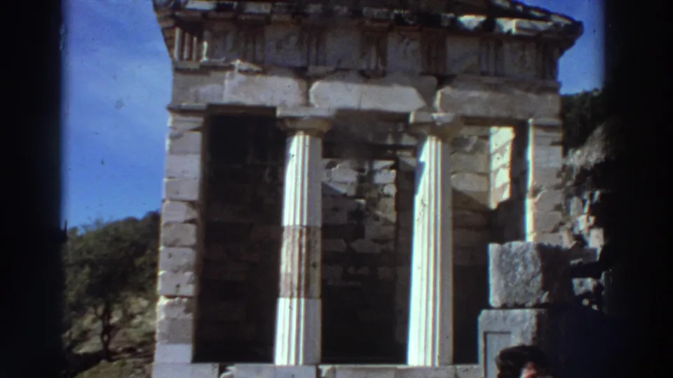 Slightly wider view of a Doric-columned treasury structure at a Greek archaeological site, circa 1976, with hillside trees visible at left.
