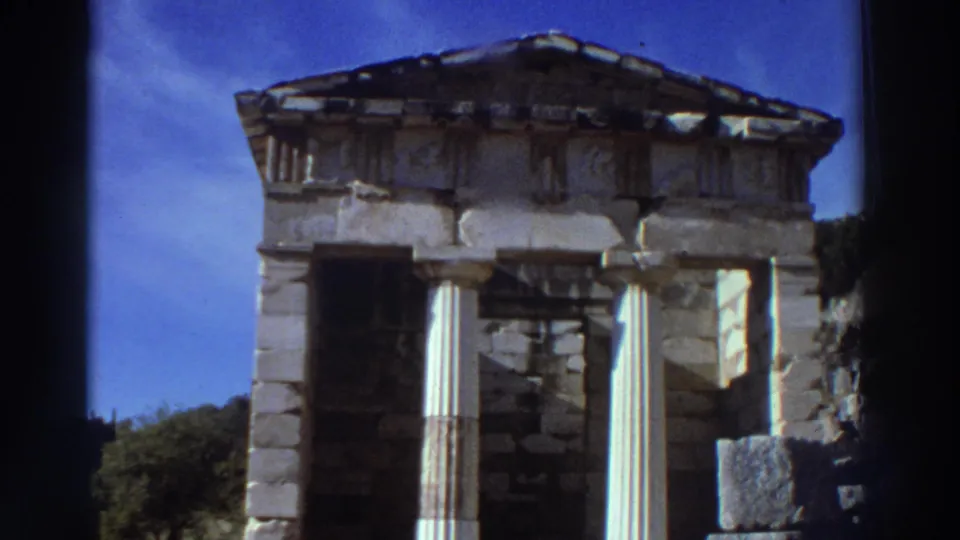 Frontal view of a Doric-columned ancient treasury at a Greek archaeological site, circa 1976; triangular pediment and upper stonework visible against clear blue sky.