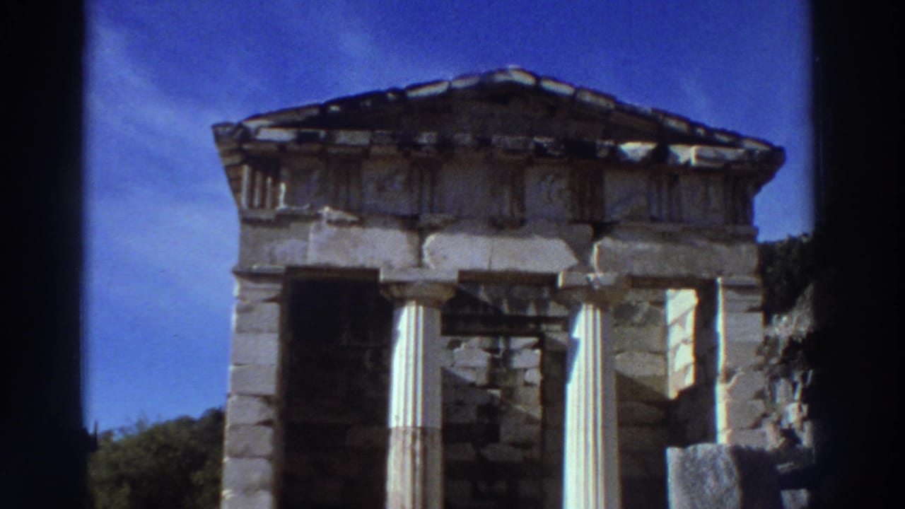 Small Doric treasury-style Greek temple structure with columns and pediment, filmed on 8mm in Greece in 1976 against a vivid blue sky.