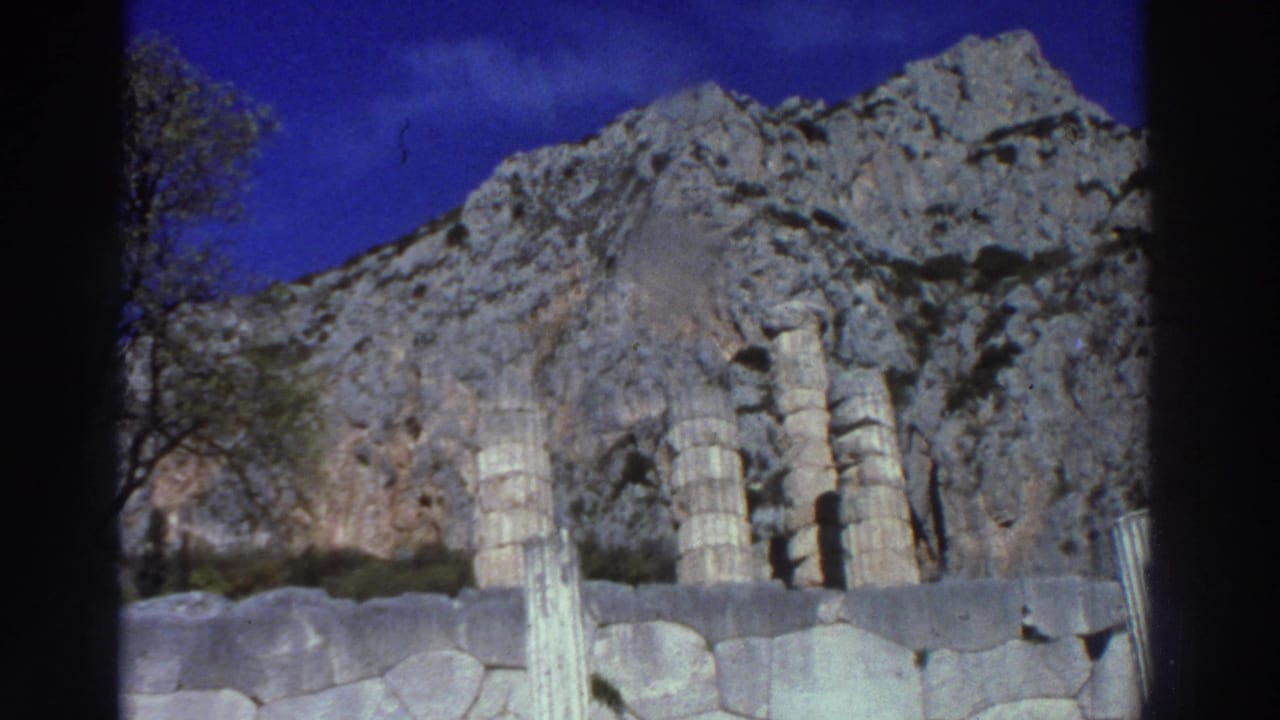 Row of ancient column drum stumps against a towering limestone cliff face and blue sky.