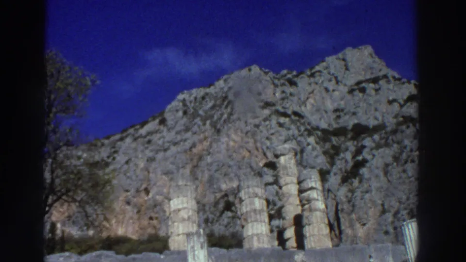 Row of ancient column remains set against a dramatic rocky mountain backdrop at a Greek site, filmed on 8mm in 1976.