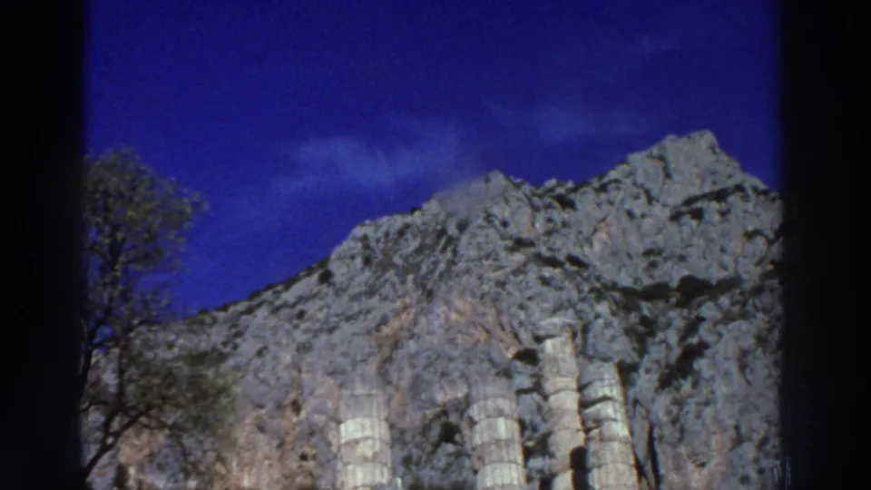 Continuation of a slow pan across ancient column remnants and rocky cliff face at a Greek archaeological site, filmed on 8mm circa 1976.