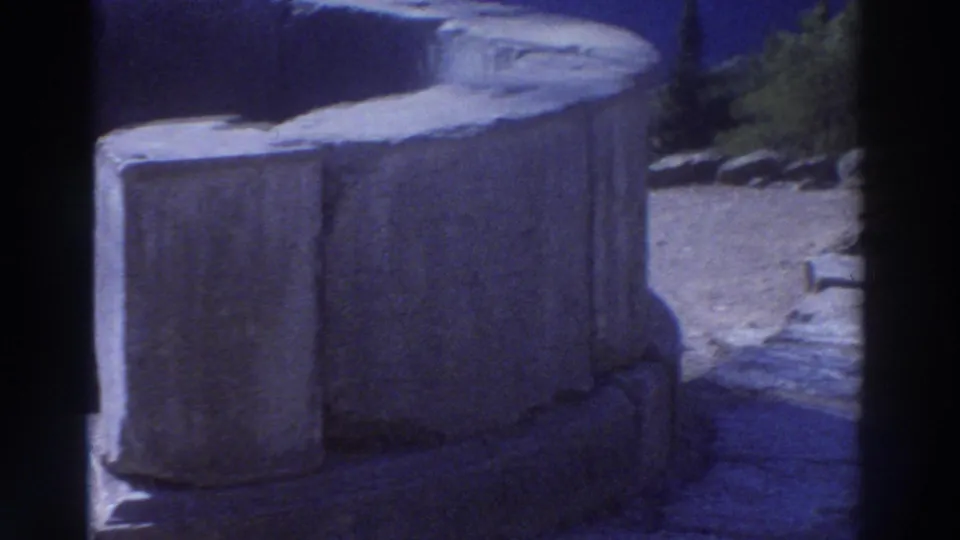 Close view of massive ancient stone column drum sections on a paved terrace at a Greek archaeological site, filmed on 8mm circa 1976.
