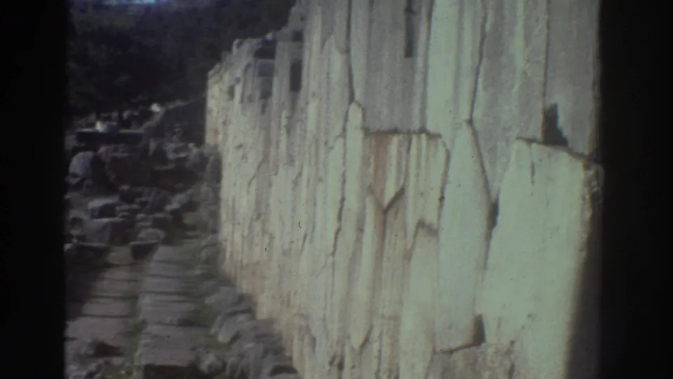 8mm home movie frame from Greece, c.1976, showing a close-up of a large ancient stone wall with weathered, cracked block surfaces and coursework.