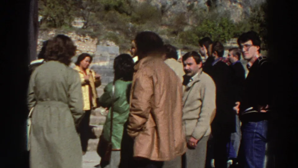 Tourists in 1970s trench coats, jeans, and sweaters standing together at the Temple of Apollo site, Greece, 1976.