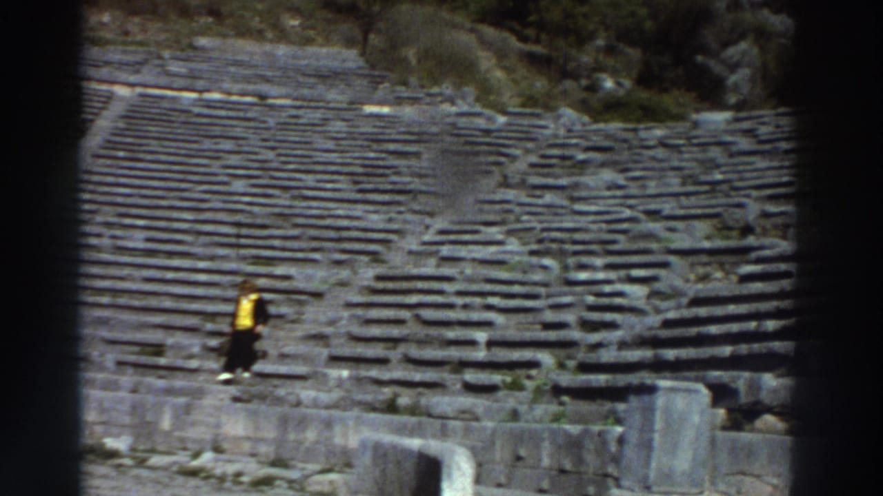 Tourist in yellow jacket climbing stone steps of an ancient amphitheater; tiered stone rows fill most of the frame.