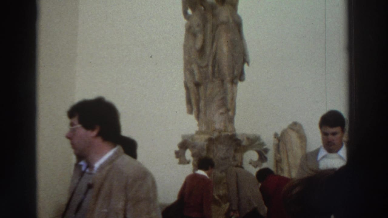 1970s Greece — museum gallery interior with classical marble statue on pedestal; male tourist in brown jacket and other visitors in foreground.