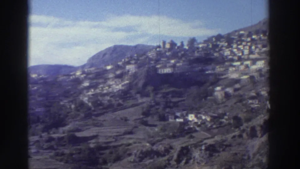 Greek mountain village on a terraced hillside, circa 1976, with whitewashed houses on dry rocky slopes; Super 8 footage with violet color shift.