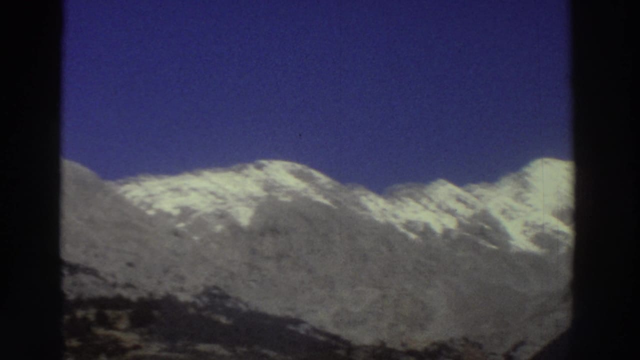 Snow-capped Greek mountain range under deep blue sky, filmed from a moving car window on 8mm film, circa 1976.