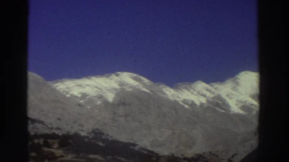 Snow-capped Greek mountain range under deep blue sky, filmed from a moving car window on 8mm film, circa 1976.
