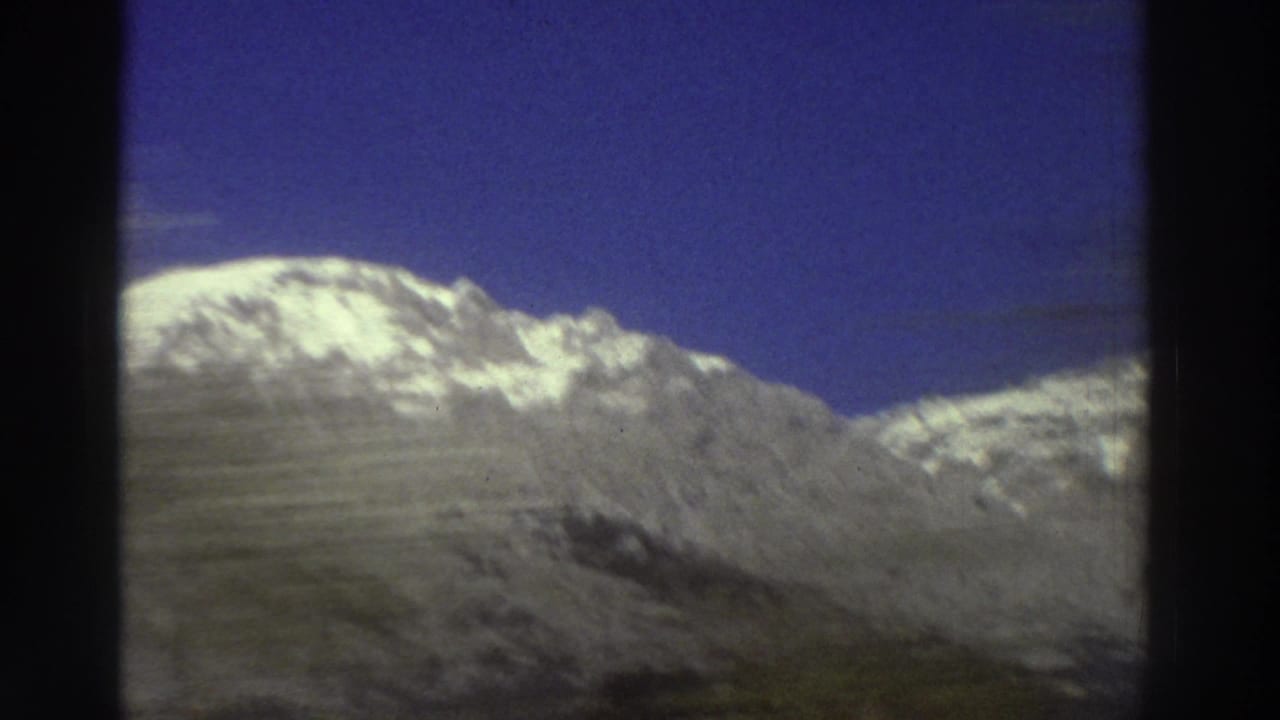 Snow-covered Greek mountain peak under vivid blue sky during a car-window pan, 8mm film, circa 1976.