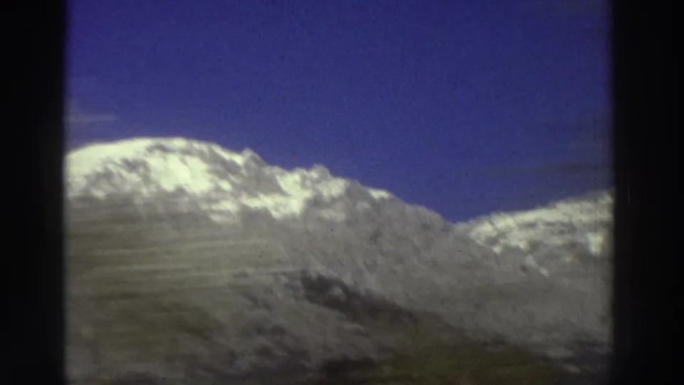 Snow-covered Greek mountain peak under vivid blue sky during a car-window pan, 8mm film, circa 1976.