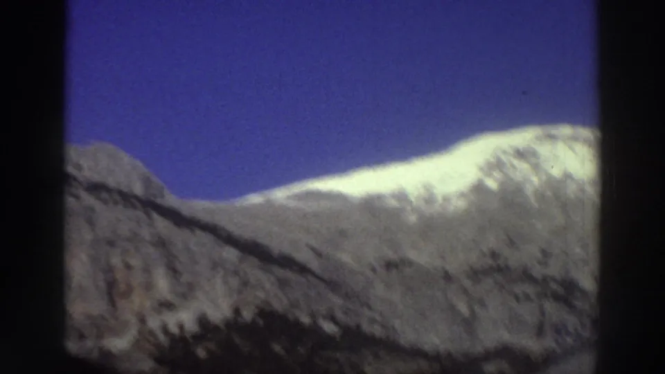 Snow-covered mountain slope in Greece, filmed from a car window against a clear blue sky, 8mm, circa 1976.