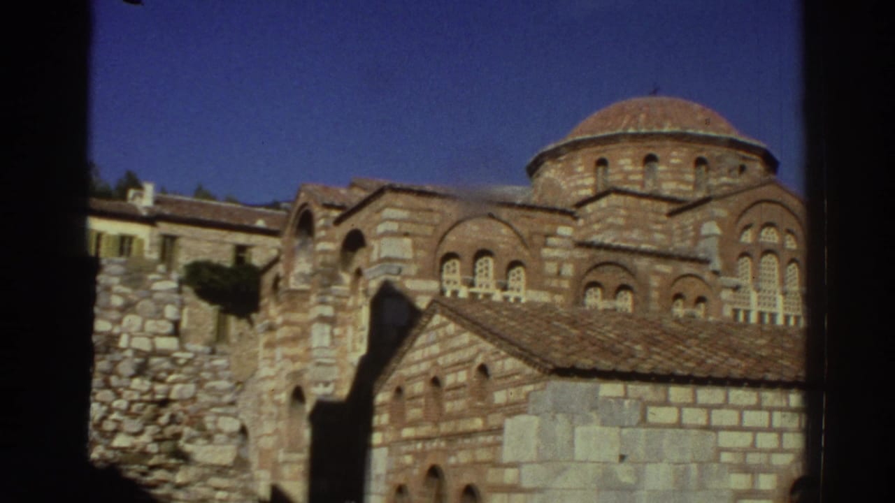Mid-pan view of a Byzantine church in Greece circa 1976, revealing twin domes, grouped arched windows, and alternating light and dark stone masonry
