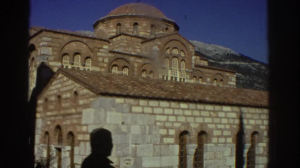 Final pan frame of a Byzantine church in Greece, 1976; main dome and stone walls with a visitor's shadow prominent in the lower foreground and hills behind