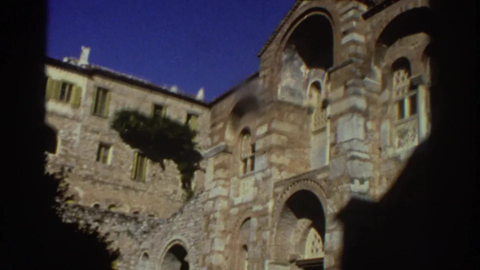Wider view of the Byzantine-style stone church exterior in Greece, 1976, showing multiple tiers of arched windows and carved stonework.