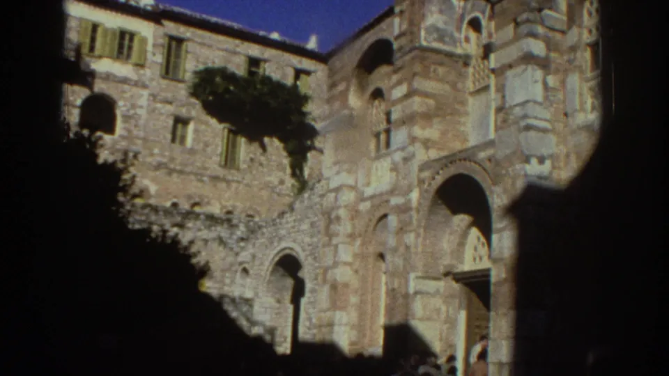 Camera panning down the Byzantine church in Greece reveals ground-level stone arches, with a large foreground shadow partially blocking the view.
