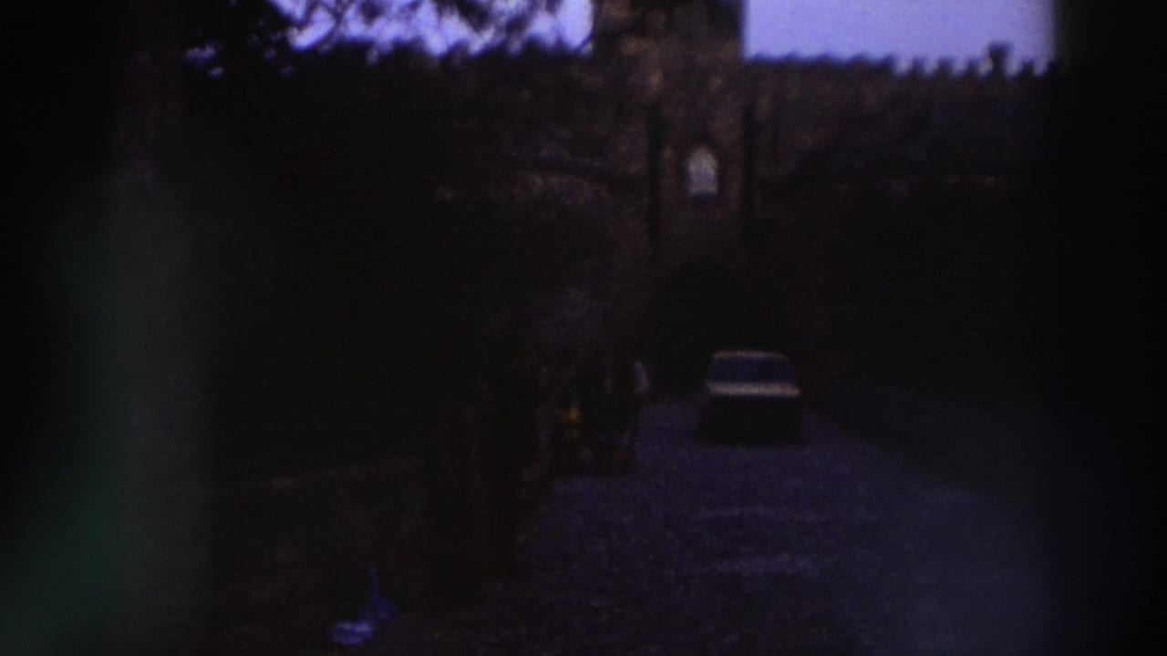 8mm home movie c.1976, Greece — light sedan near a crenellated stone gateway, deep purple-blue dye shift, dark foreground vignetting.