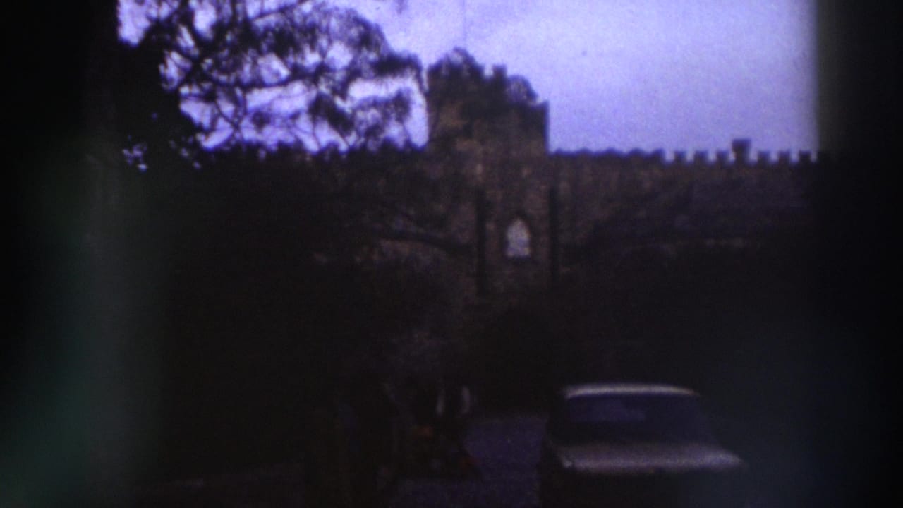 8mm frame c.1976, Greece — crenellated stone wall with a tall tree, light sedan visible to the right, film aging evident in purple-blue cast.