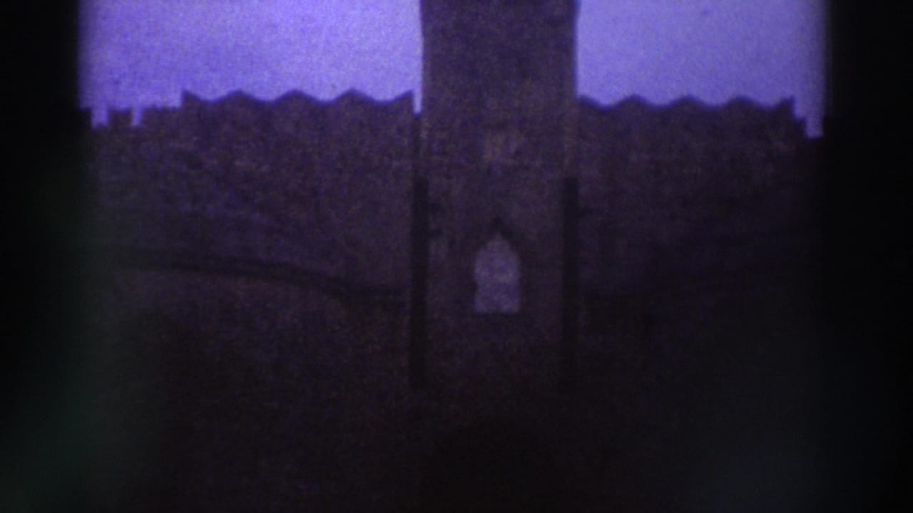 Underexposed 8mm frame with strong purple-blue color cast showing crenellated exterior walls of what appears to be a medieval stone fortification, Greece circa 1976.