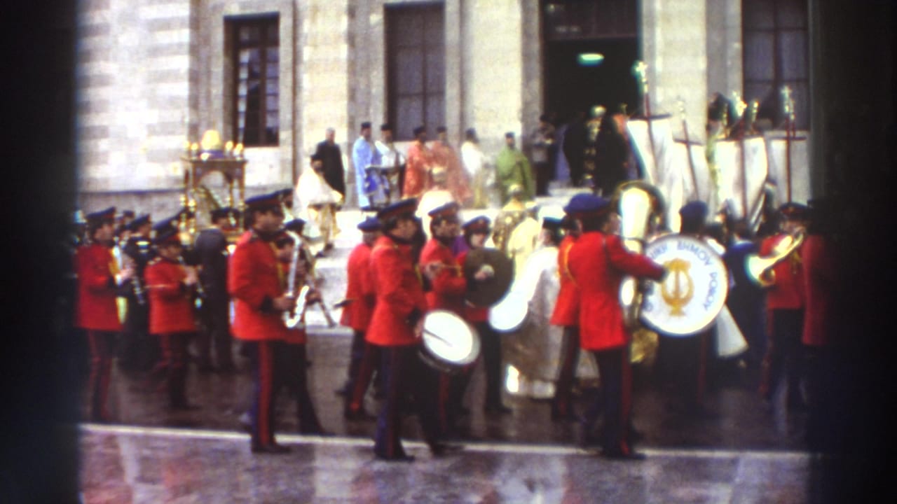 Close view of marching band in red uniforms with black kepis playing brass instruments, clergy and golden relics visible behind.