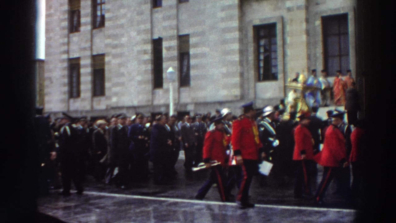 Red-coated honor guards march in formation outside a stone church facade during a Greek religious procession, circa 1976.