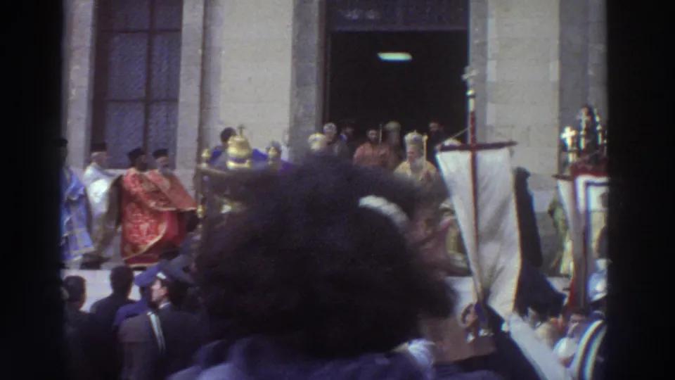 Filmed from within the crowd, a Greek Orthodox procession passes with gilded icons, crosses, and clergy in red and gold vestments, circa 1976.