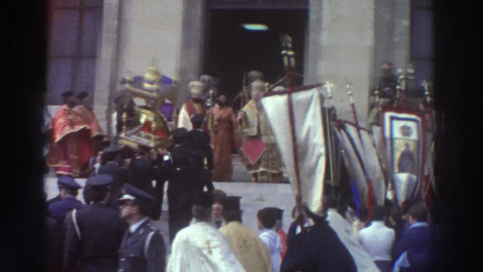 Multiple gilded icons, white banners, and clergy in gold vestments near a stone church entrance, uniformed guards visible in the foreground, circa 1976.