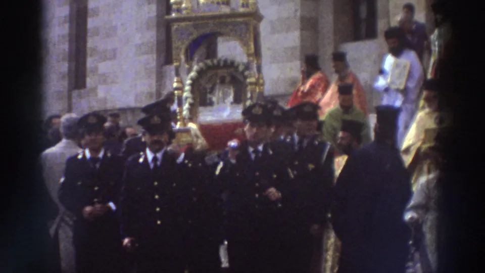 Navy-uniformed honor guards escort a gilded portable icon shrine past a stone building during a Greek Orthodox procession, Greece, circa 1976.