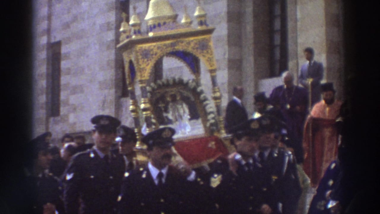 1976 Greece frame with a gilded reliquary and red platform moving through a church-side procession with uniformed men and clergy nearby.