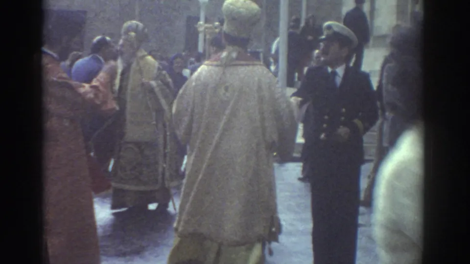 1976 Greece frame showing clergy in pale and gold vestments beside a uniformed man as the religious procession gathers near the church.