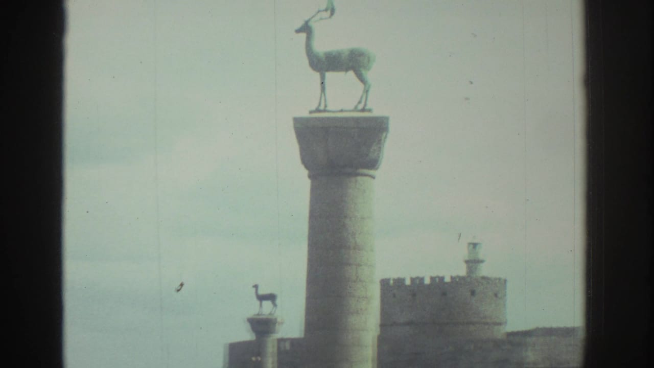 Tall column topped with a deer sculpture beside a crenellated harbor fort and another smaller column.