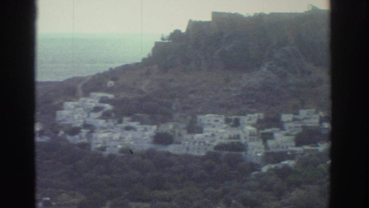 Rocky coastal village with white buildings and sea between two hills.