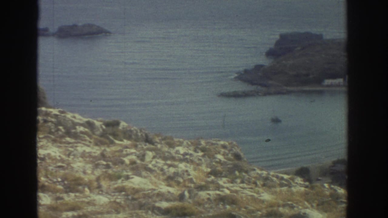 Coastal bay seen past rocky foreground with headlands and calm sea.