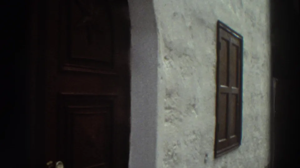 1976 Greece 8mm frame showing a whitewashed exterior wall, dark wooden door, small shuttered window, and shaded alley architecture.