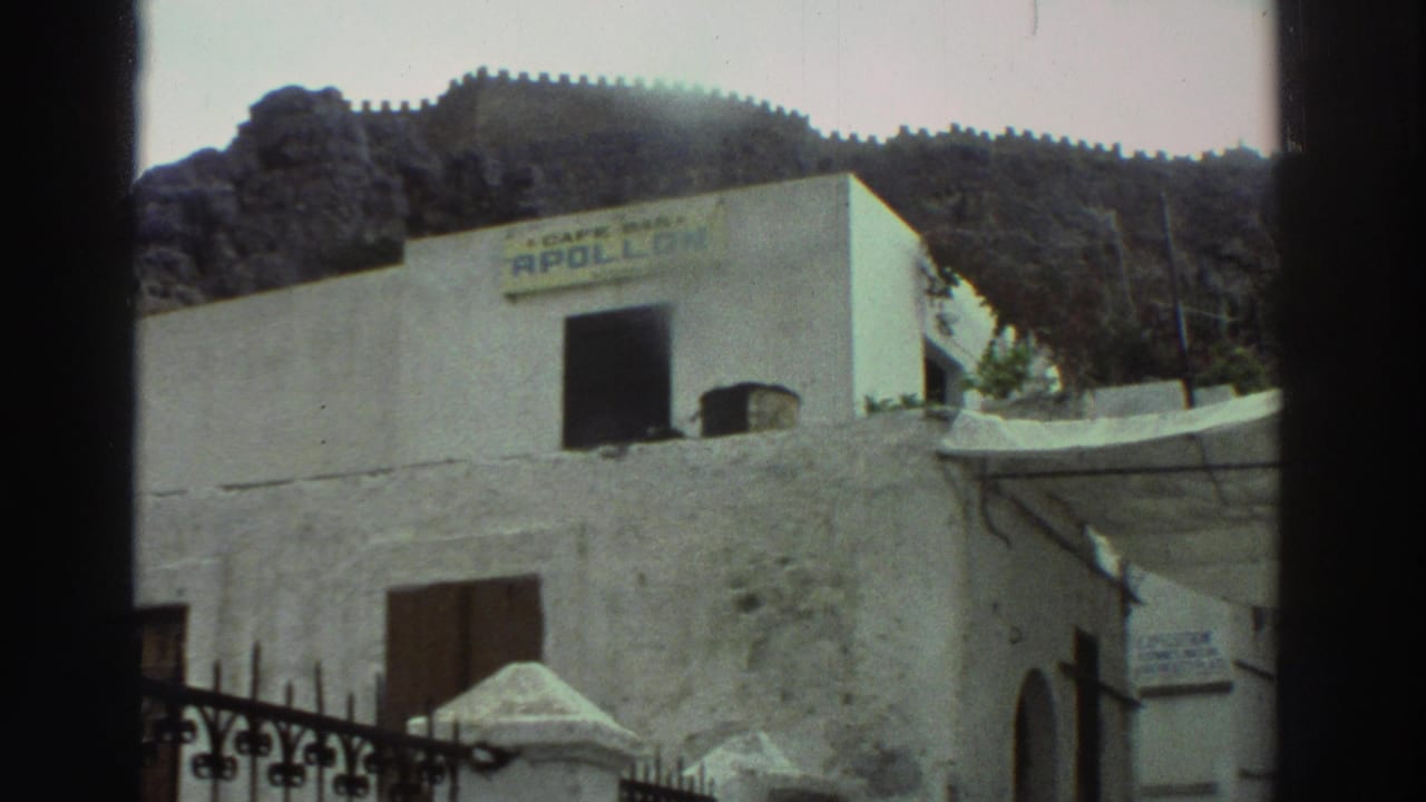 Cafe building and white walls seen behind a wrought-iron gate, with rocky hillside above.