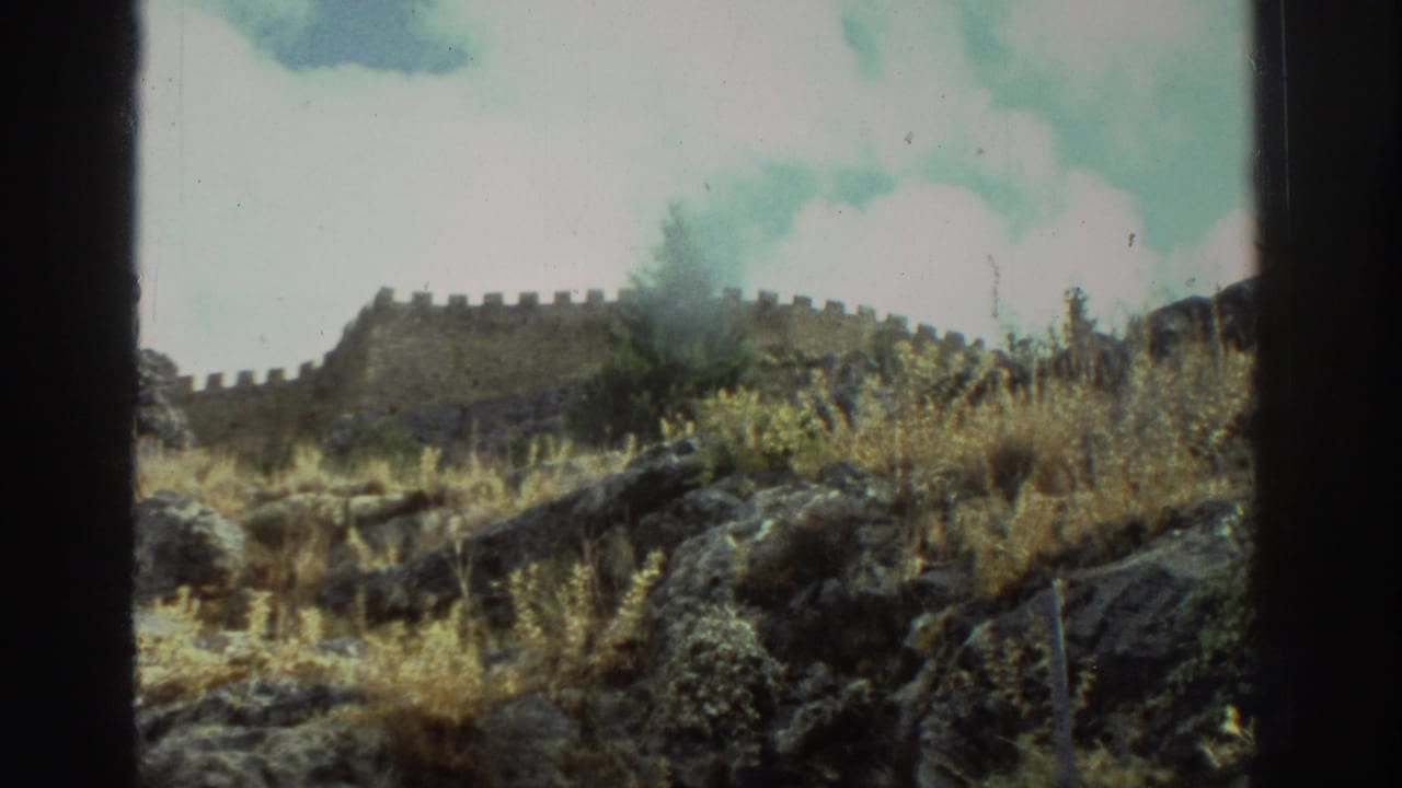 Stone battlements above a rocky, grass-covered cliffside under a pale sky.