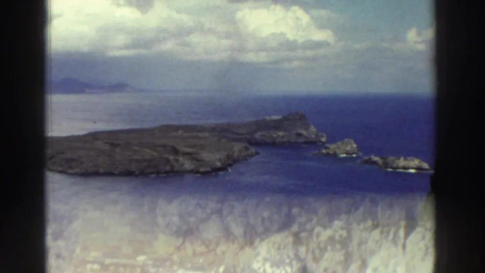 1976 Greece travel footage showing a coastal overlook with pale ancient-looking stone ruins in the foreground and blue sea beyond.